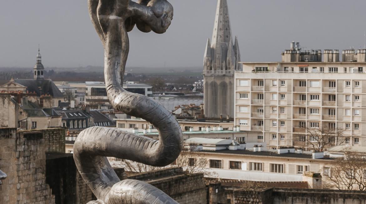 Zoom sur la sculpture du serpent à neuf têtes, qui se découpe dans un ciel bleu, juché sur son mât en bois.