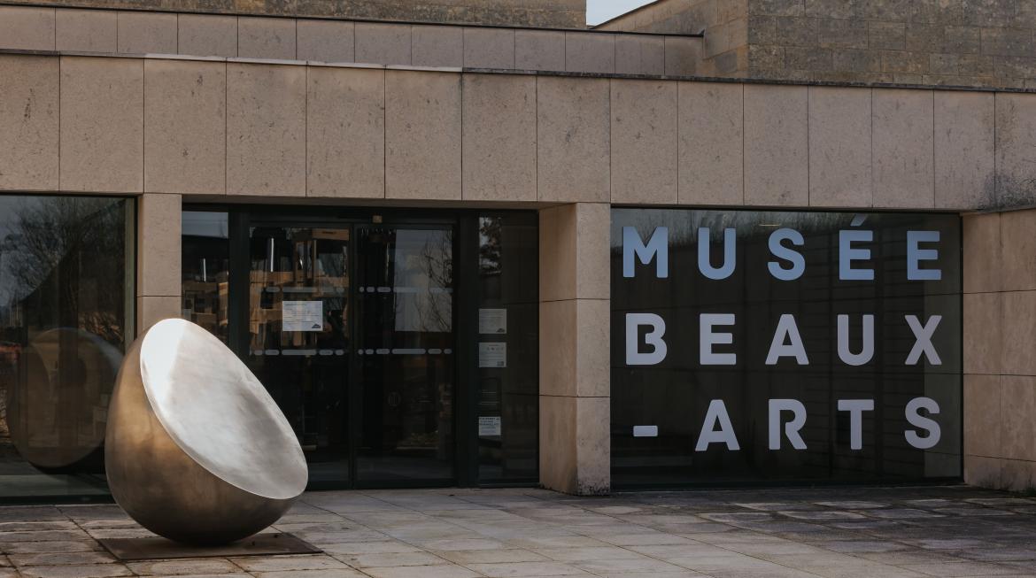 Devant l'entrée du musée des Beaux-Arts, une sphère coupée en acier est posée à gauche, au sol. Les portes sont vitrées, et sur la fenêtre de droite le nom du musée est inscrit en blanc.