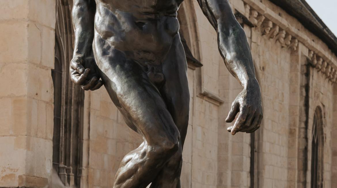 La statue de Auguste Rodin, la Grande Ombre, trône au centre de l'image. Elle est en bronze, et se trouve devant l'Église Saint Georges.