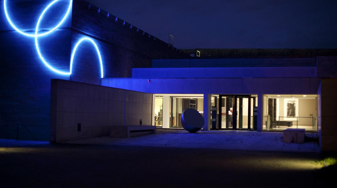 Cette vue de nuit montre la façade du musée. L'installation de Morellet, faite de néons bleus, baigne le lieu d'une lueur bleue électrique.